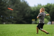 Boy throwing red frisbee away from camera in a green park. 